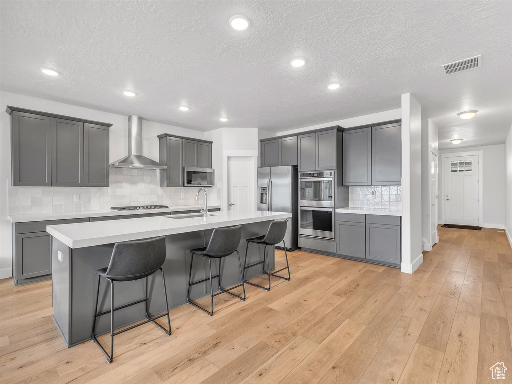 Kitchen with stainless steel appliances, visible vents, light countertops, wall chimney range hood, and a kitchen bar