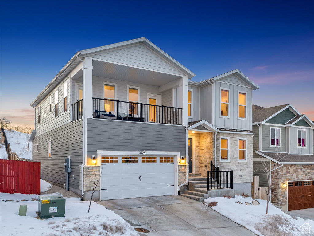 View of front of house with a balcony, a garage, stone siding, concrete driveway, and board and batten siding