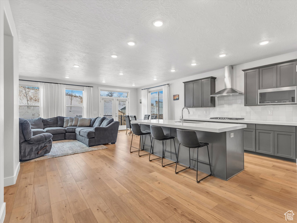 Kitchen with wall chimney exhaust hood, a breakfast bar area, open floor plan, light countertops, and a center island with sink