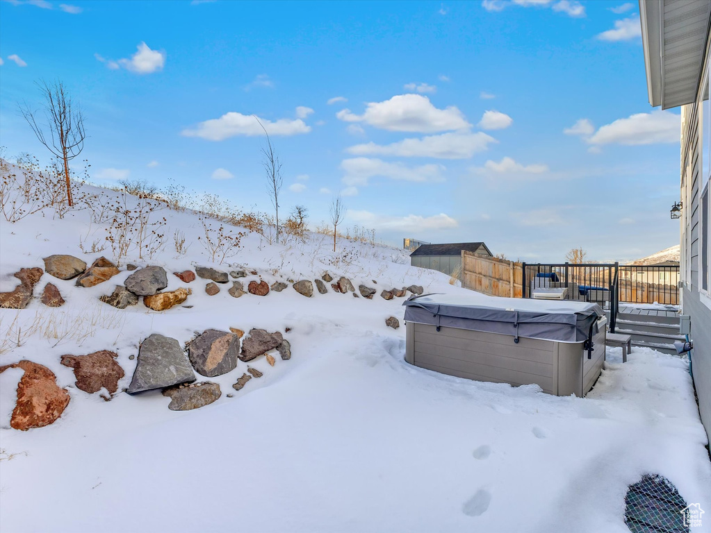 Yard layered in snow featuring fence, a garage, and a hot tub