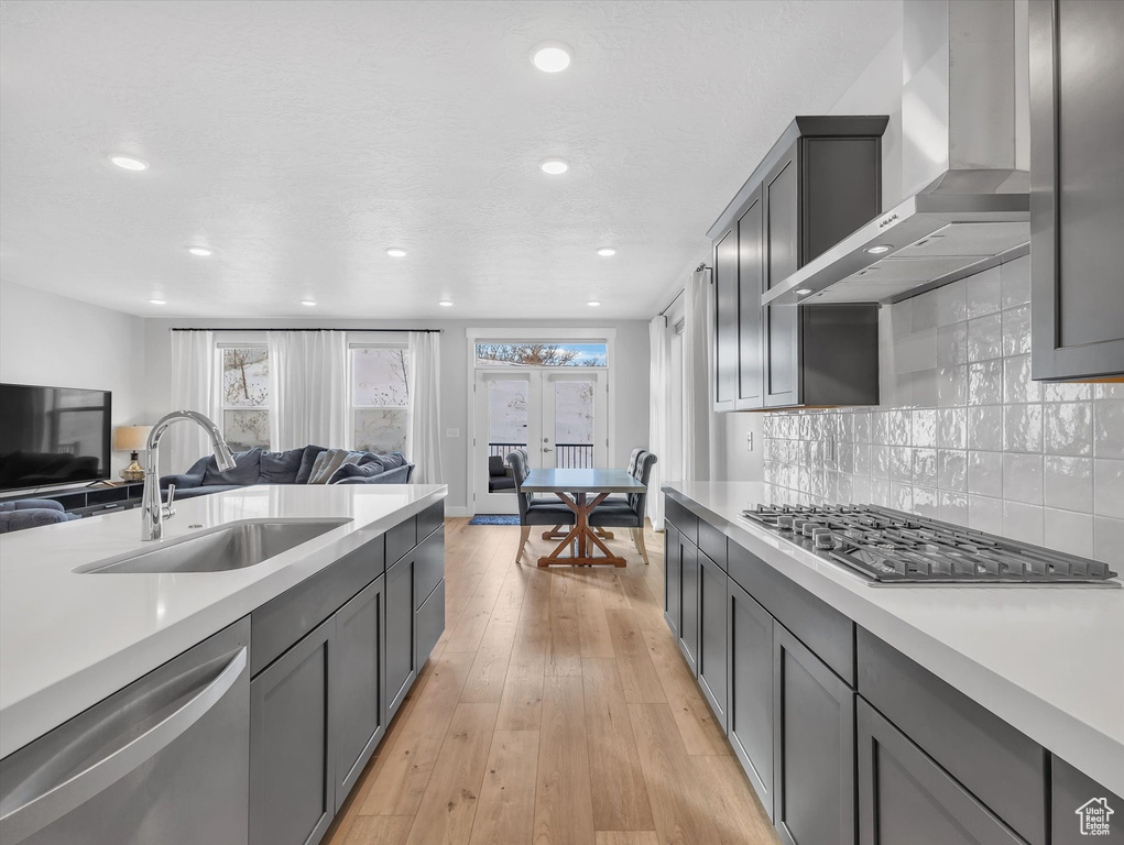 Kitchen featuring wall chimney exhaust hood, appliances with stainless steel finishes, open floor plan, and light countertops