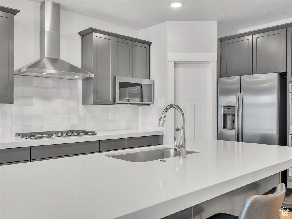 Kitchen featuring a sink, a breakfast bar area, wall chimney range hood, light countertops, and appliances with stainless steel finishes