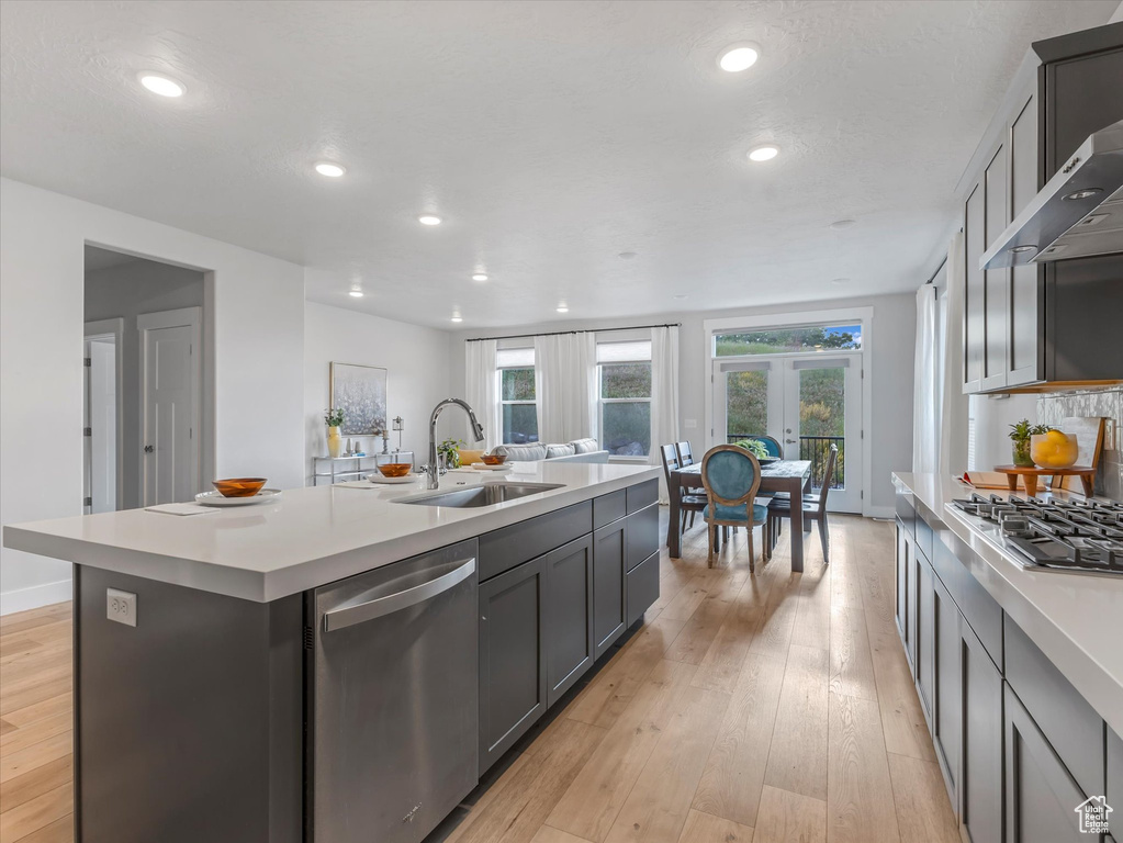 Kitchen featuring appliances with stainless steel finishes, wall chimney range hood, light countertops, an island with sink, and recessed lighting