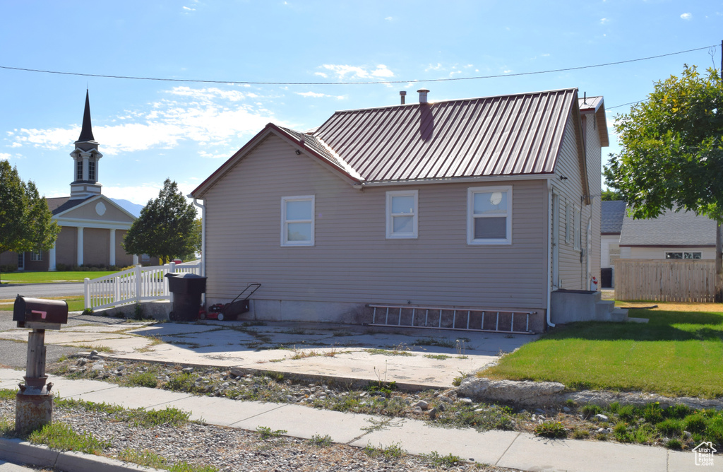 View of property exterior featuring fence, metal roof, and a lawn