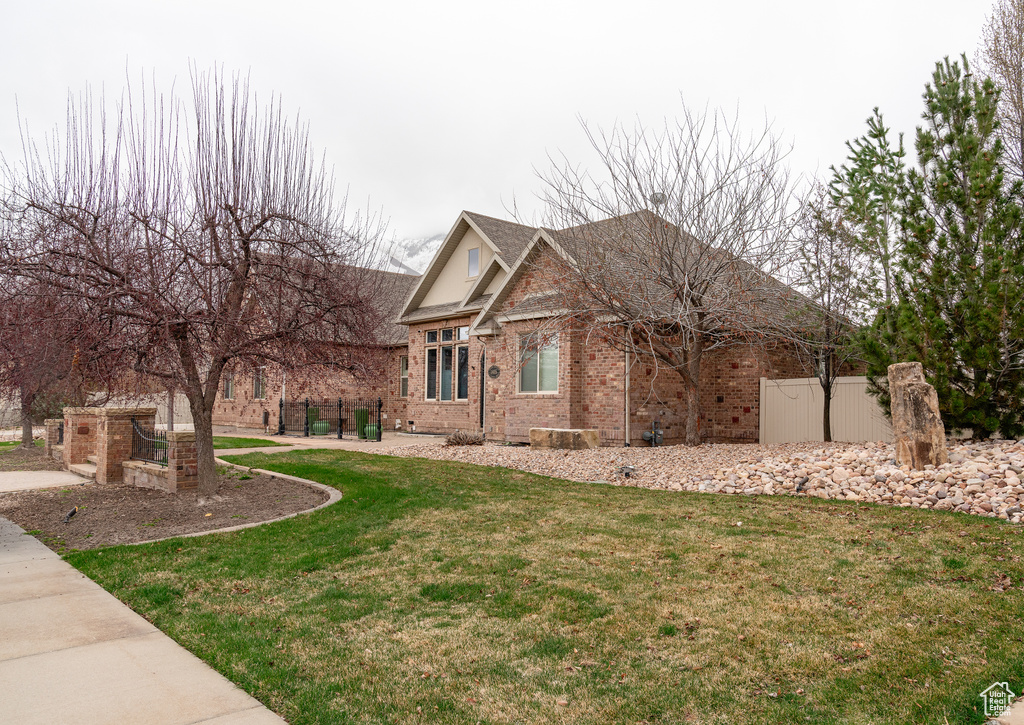 View of side of home with brick siding, a shingled roof, fence, and a lawn