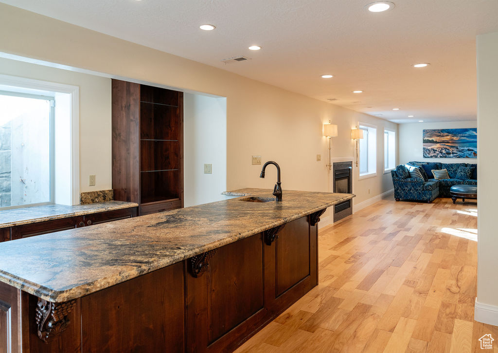 Kitchen featuring sink, a kitchen island with sink, light wood-type flooring, and light stone counters