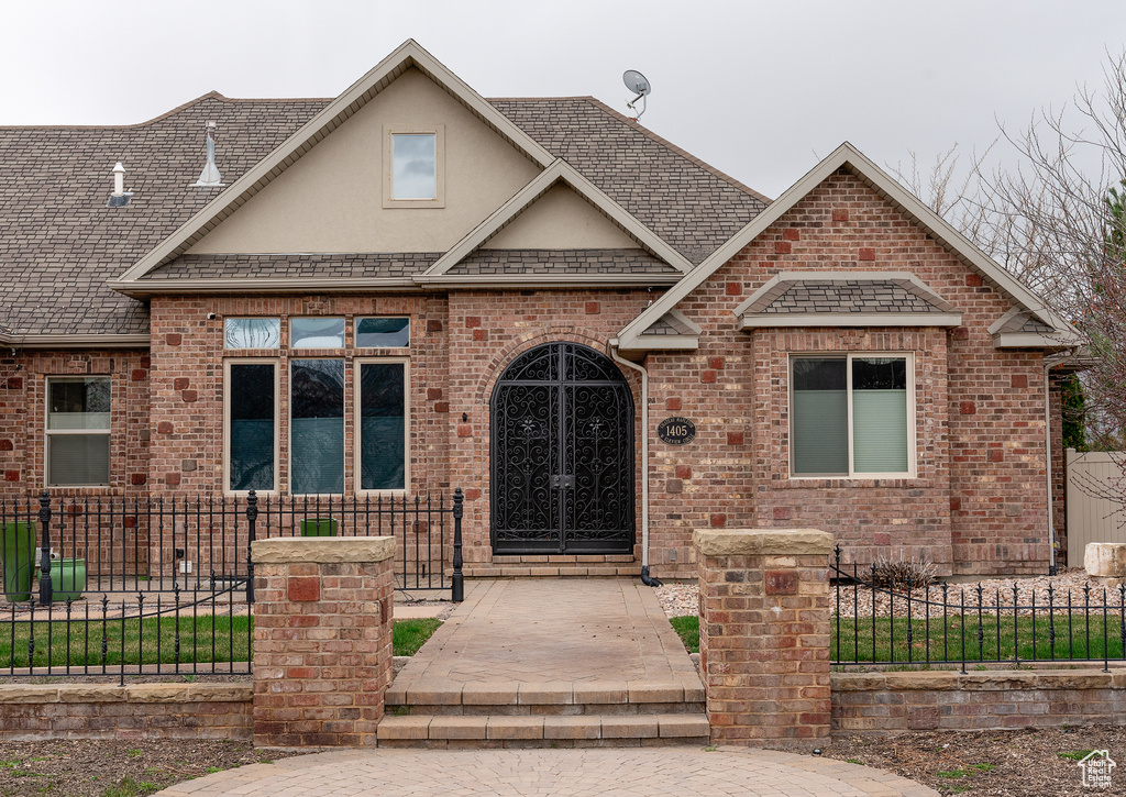View of front facade featuring stucco siding, brick siding, a shingled roof, and a fenced front yard