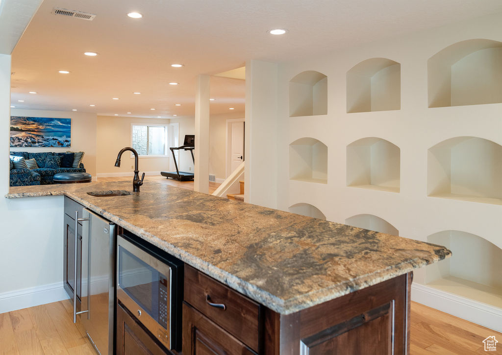 Kitchen featuring light wood-type flooring, dark brown cabinets, sink, and light stone counters