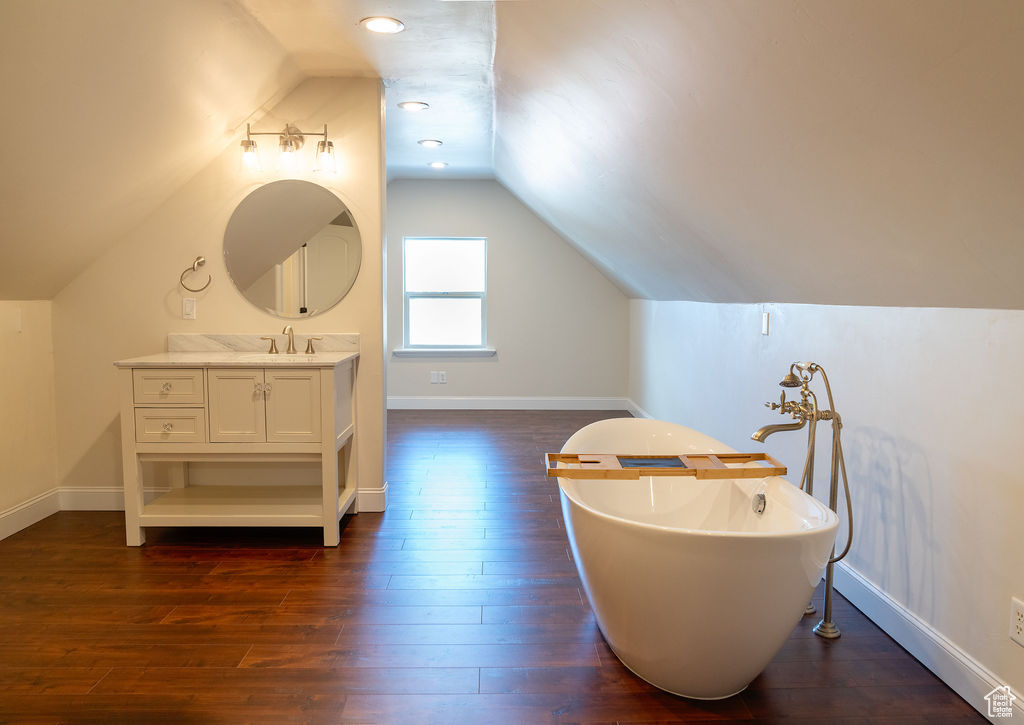 Bathroom featuring vanity, hardwood / wood-style floors, a washtub, and vaulted ceiling