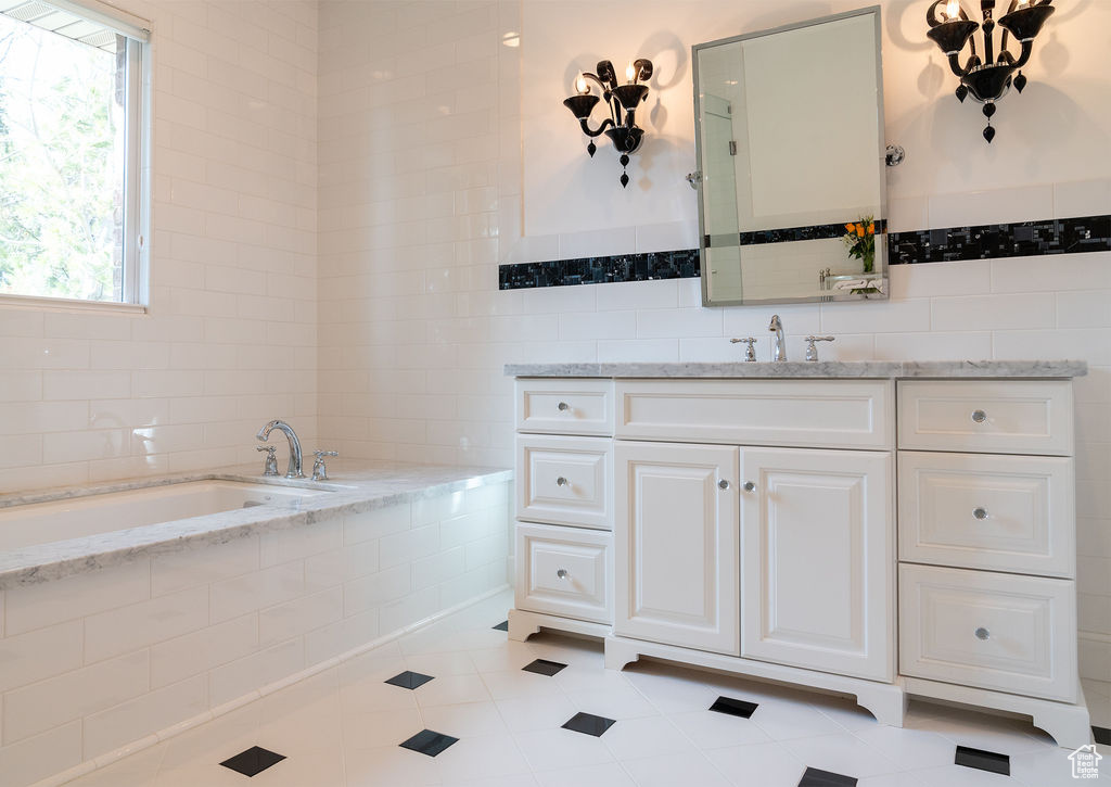Bathroom with tile patterned floors, tile walls, vanity, and a relaxing tiled tub