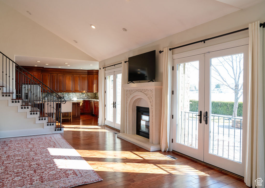 Unfurnished living room with light hardwood / wood-style flooring, vaulted ceiling, french doors, and a healthy amount of sunlight