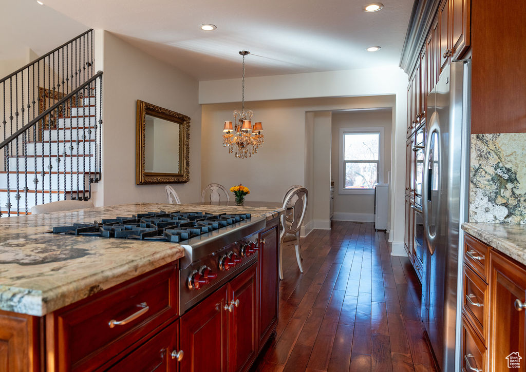 Kitchen with a notable chandelier, dark hardwood / wood-style floors, stainless steel appliances, hanging light fixtures, and light stone countertops