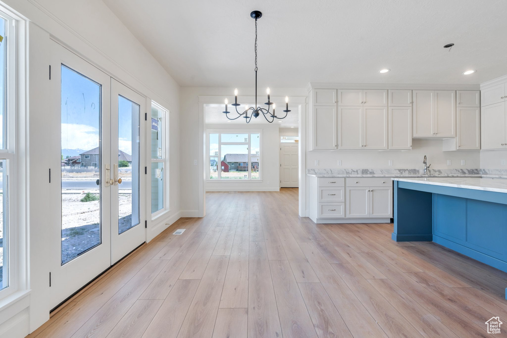 Kitchen featuring a chandelier, white cabinetry, pendant lighting, light wood-type flooring, and french doors