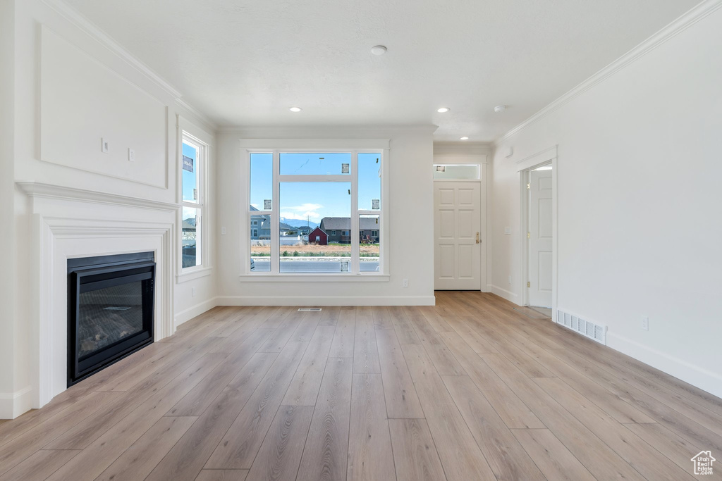 Unfurnished living room featuring crown molding, light wood-type flooring, a glass covered fireplace, and recessed lighting