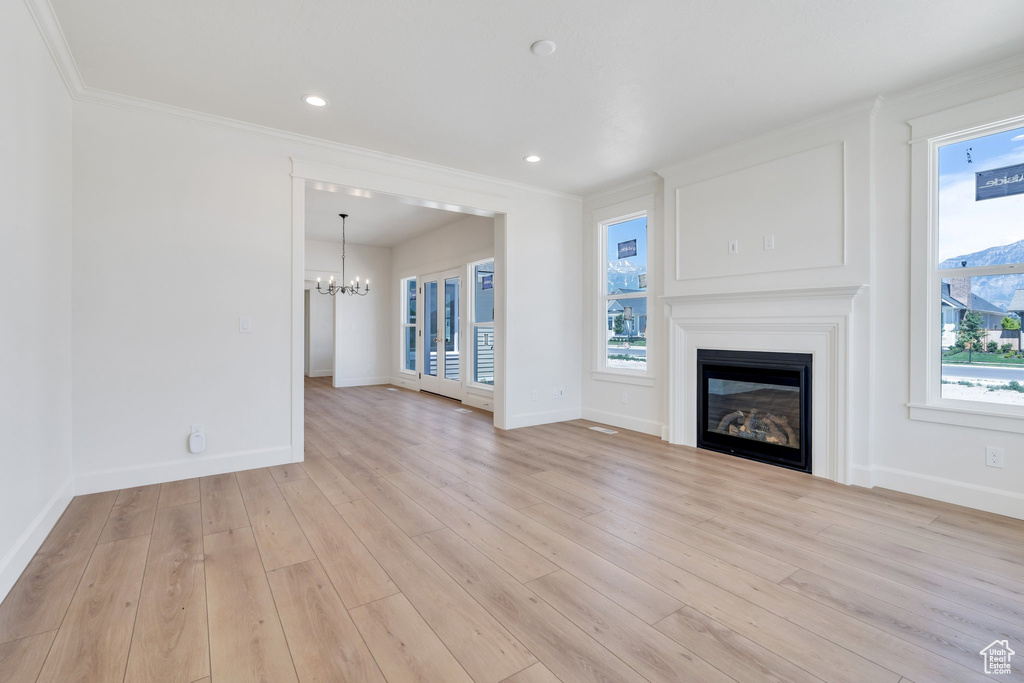 Unfurnished living room featuring a chandelier, a glass covered fireplace, ornamental molding, light wood finished floors, and recessed lighting