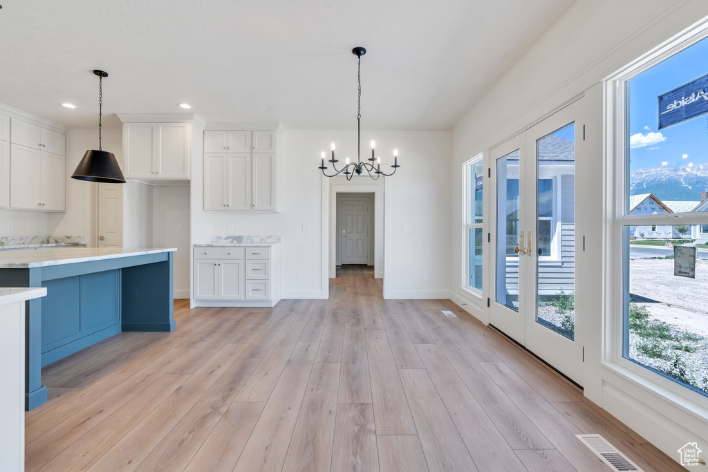 Kitchen featuring a chandelier, white cabinetry, light wood-type flooring, light countertops, and pendant lighting