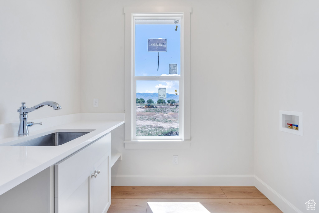 Laundry room with light wood-style floors, washer hookup, and cabinet space