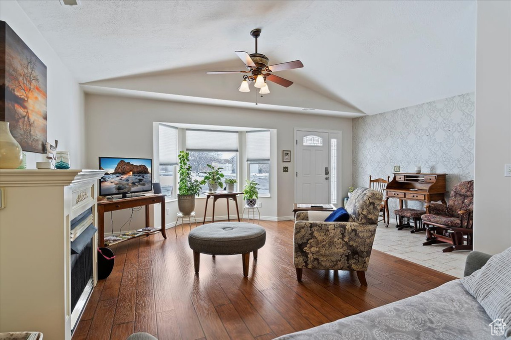 Interior space with light wood finished floors, wallpapered walls, baseboards, lofted ceiling, and an accent wall
