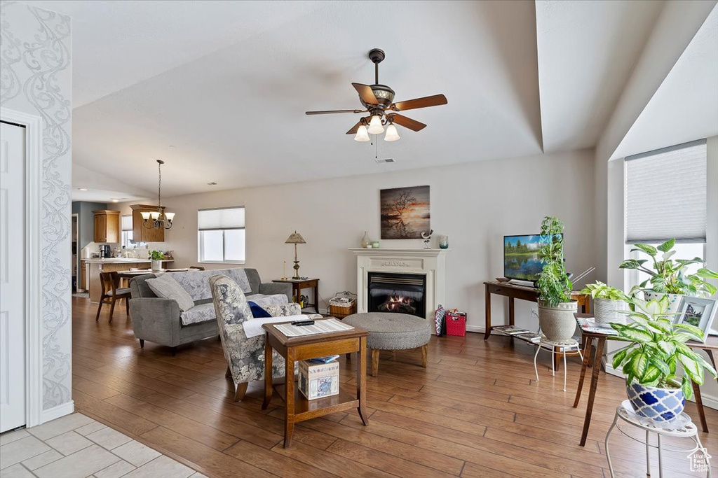 Living room with light wood finished floors, baseboards, ceiling fan with notable chandelier, and a glass covered fireplace