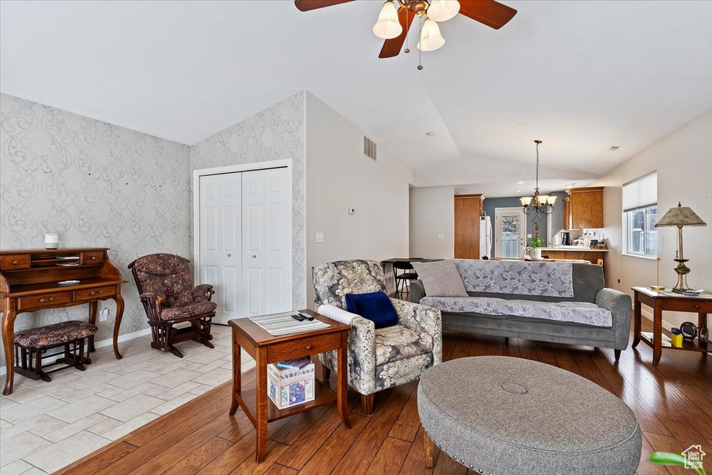 Living area with light wood-type flooring, lofted ceiling, visible vents, and wallpapered walls