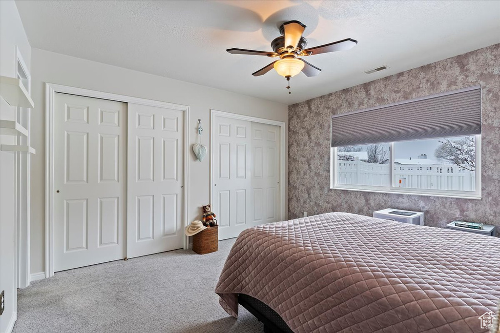 Bedroom with two closets, light colored carpet, visible vents, a ceiling fan, and a textured ceiling