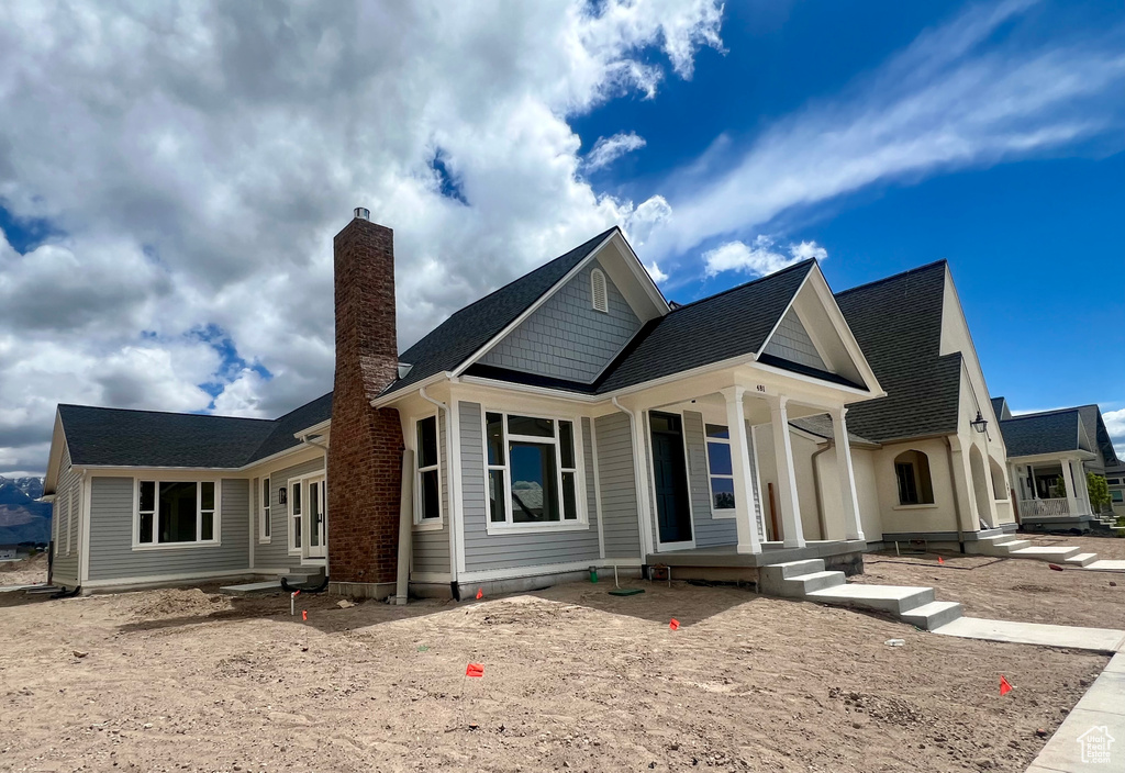 View of front of house with a chimney, a porch, and roof with shingles