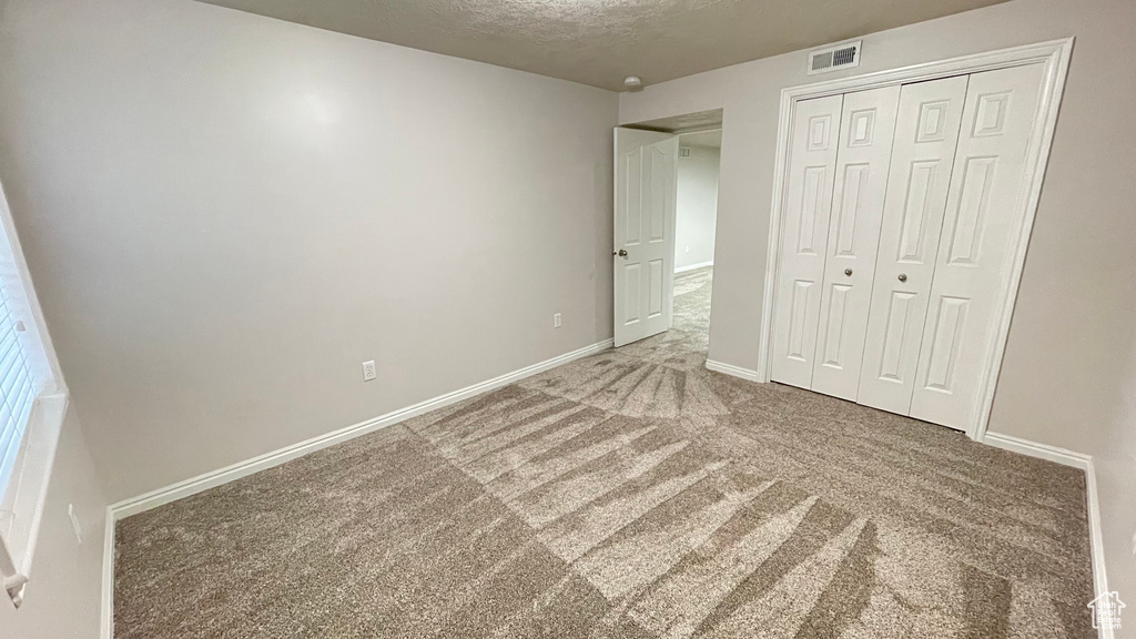 Unfurnished bedroom with carpet flooring, a closet, a textured ceiling, and baseboards