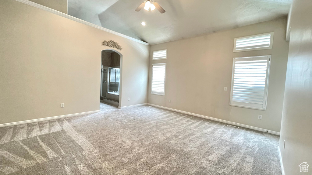 Carpeted empty room featuring arched walkways, ceiling fan, baseboards, and lofted ceiling