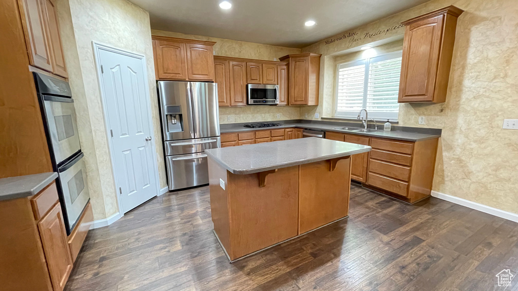 Kitchen featuring appliances with stainless steel finishes, a sink, a center island, dark wood-style flooring, and a breakfast bar