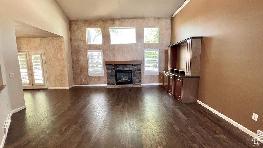 Unfurnished living room featuring a high ceiling, baseboards, a fireplace, and dark wood finished floors