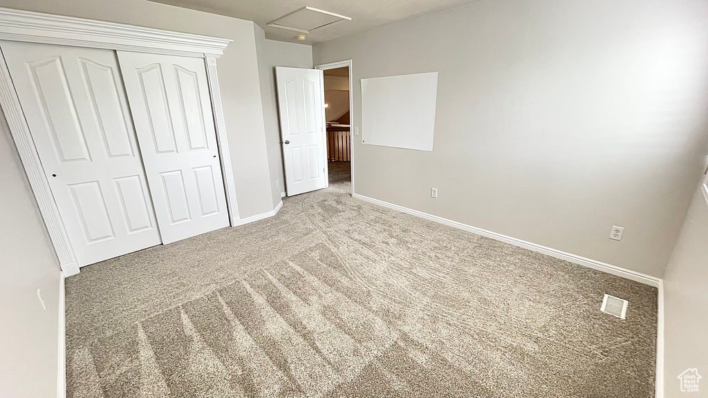 Unfurnished bedroom with carpet floors, a closet, baseboards, and attic access