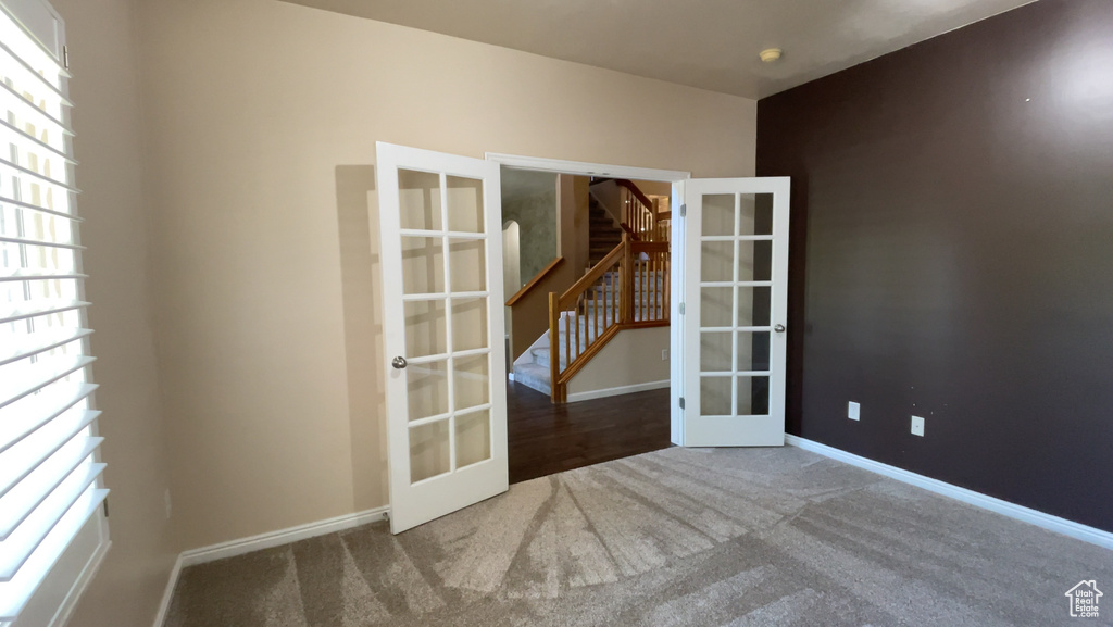 Spare room featuring french doors, carpet flooring, stairs, and baseboards