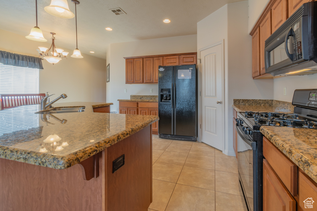 Kitchen featuring hanging light fixtures, brown cabinetry, a kitchen island with sink, a sink, and black appliances