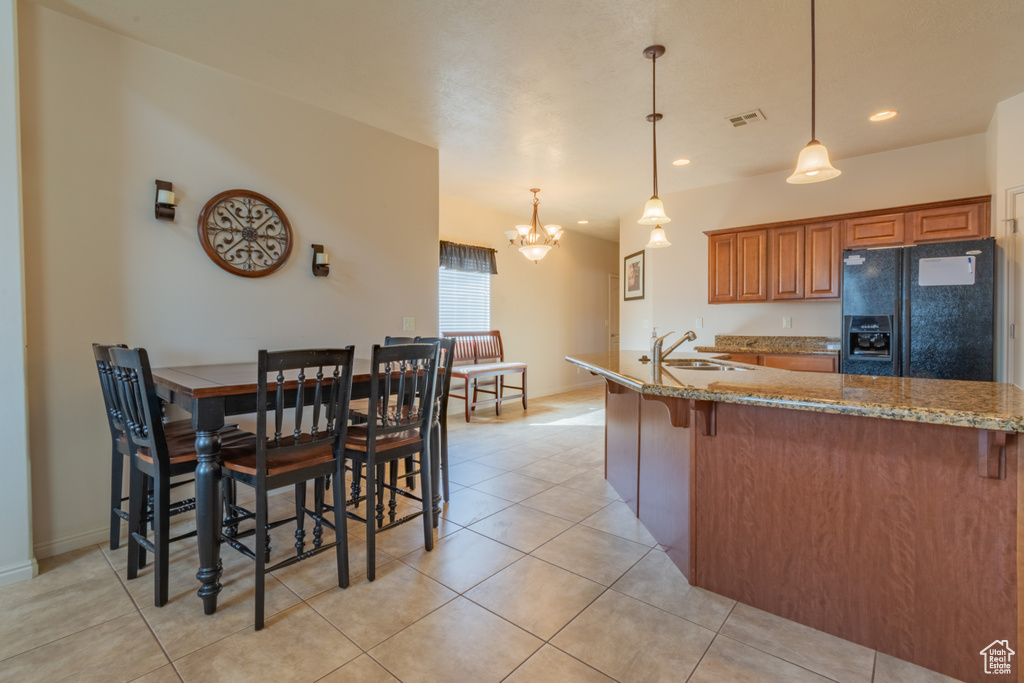 Kitchen featuring light stone counters, visible vents, hanging light fixtures, black fridge, and brown cabinetry