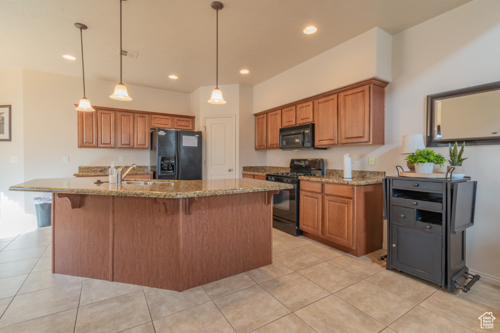 Kitchen with a sink, brown cabinets, black appliances, an island with sink, and pendant lighting