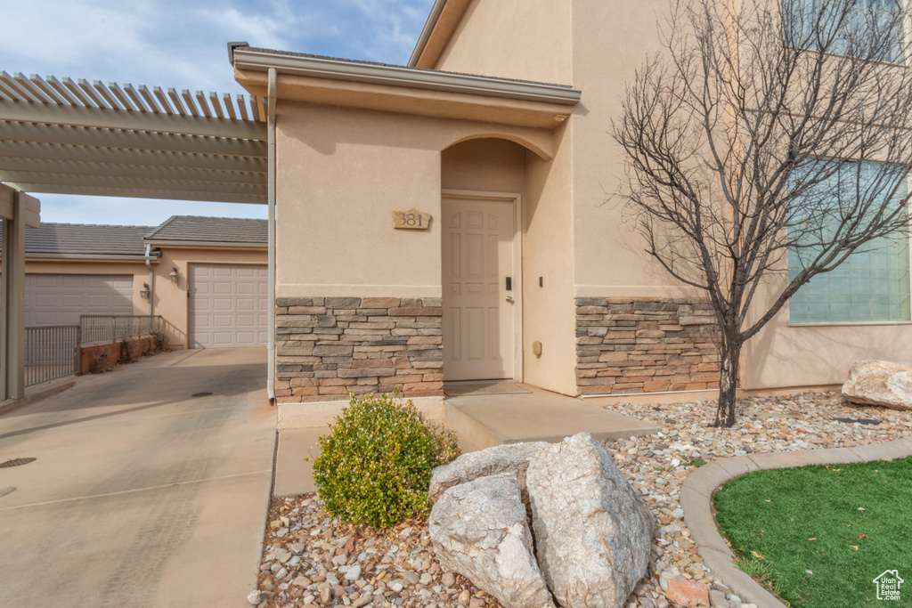 View of exterior entry featuring stone siding, concrete driveway, a pergola, and stucco siding