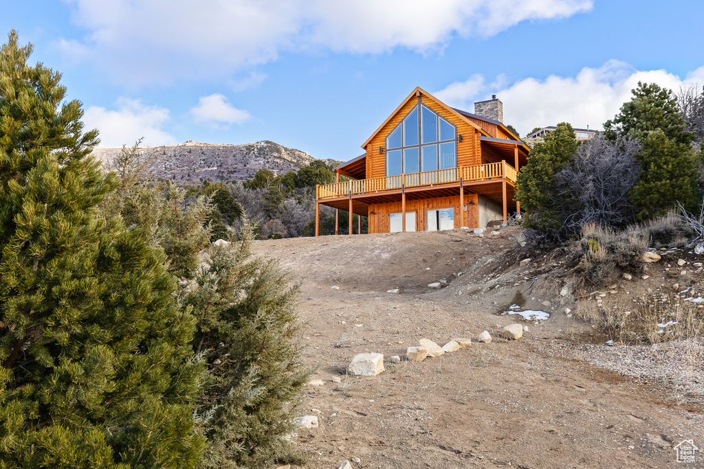 Exterior space featuring a deck with mountain view, driveway, an attached garage, and a chimney