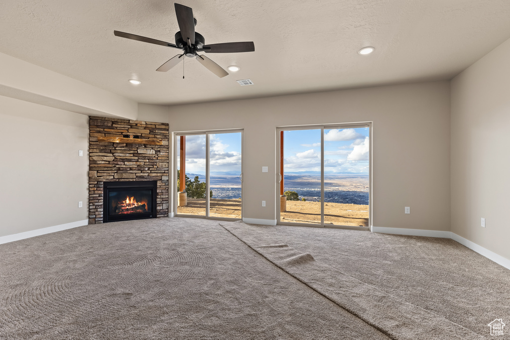 Unfurnished living room with a textured ceiling, carpet floors, a fireplace, visible vents, and baseboards