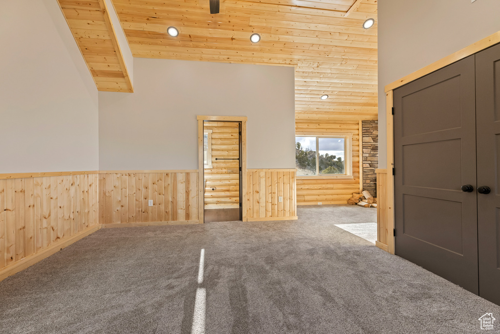 Carpeted spare room featuring high vaulted ceiling, wood ceiling, a wainscoted wall, and wooden walls