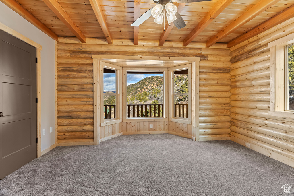 Empty room featuring rustic walls, wood ceiling, ceiling fan, and beamed ceiling