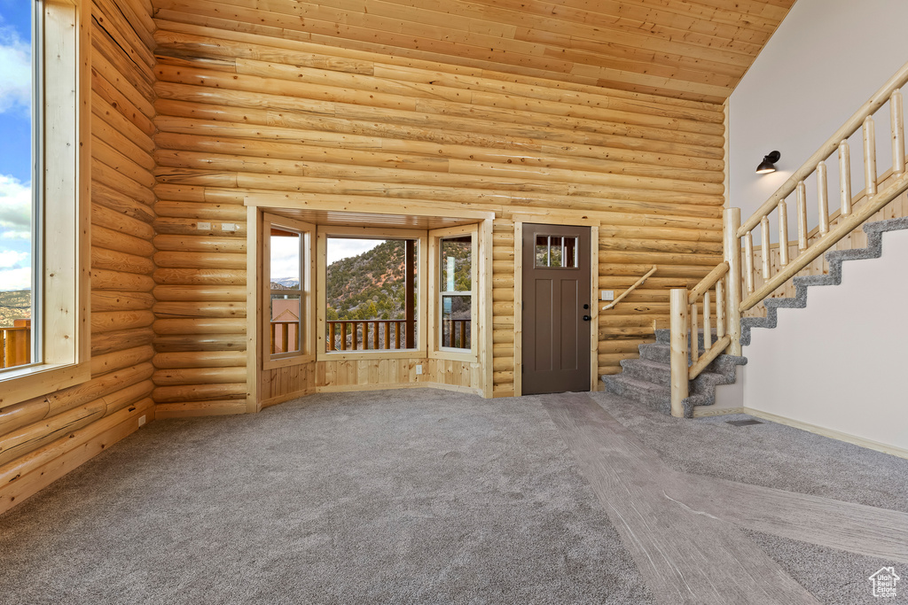 Unfurnished living room featuring high vaulted ceiling, rustic walls, plenty of natural light, and stairs