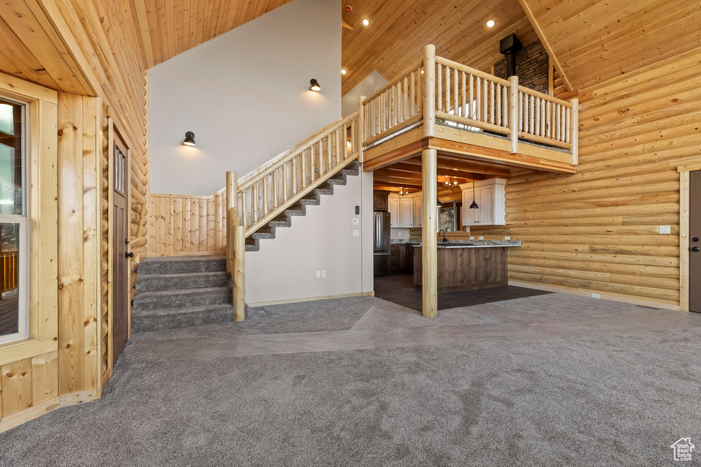 Unfurnished living room featuring high vaulted ceiling, dark colored carpet, wood ceiling, and stairway