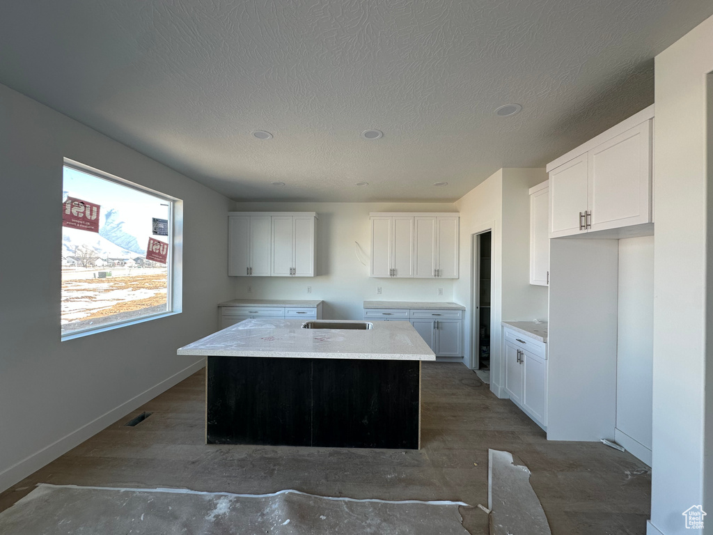 Kitchen with a textured ceiling, a kitchen island, visible vents, baseboards, and white cabinets