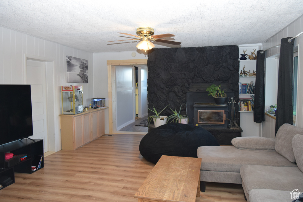 Living area featuring a ceiling fan, a stone fireplace, a textured ceiling, and light wood finished floors