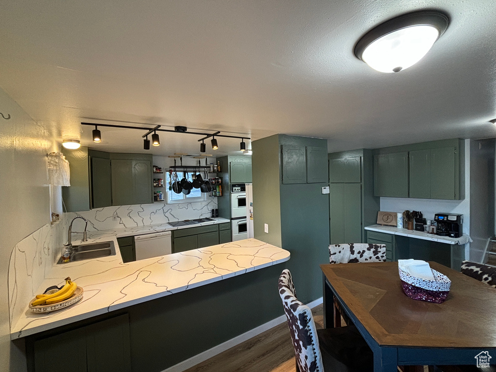 Kitchen with a peninsula, white appliances, green cabinetry, and a sink