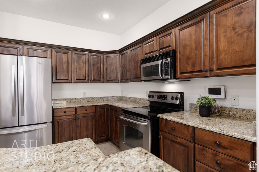 Kitchen with stainless steel appliances, light tile patterned flooring, light stone counters, dark brown cabinets, and recessed lighting