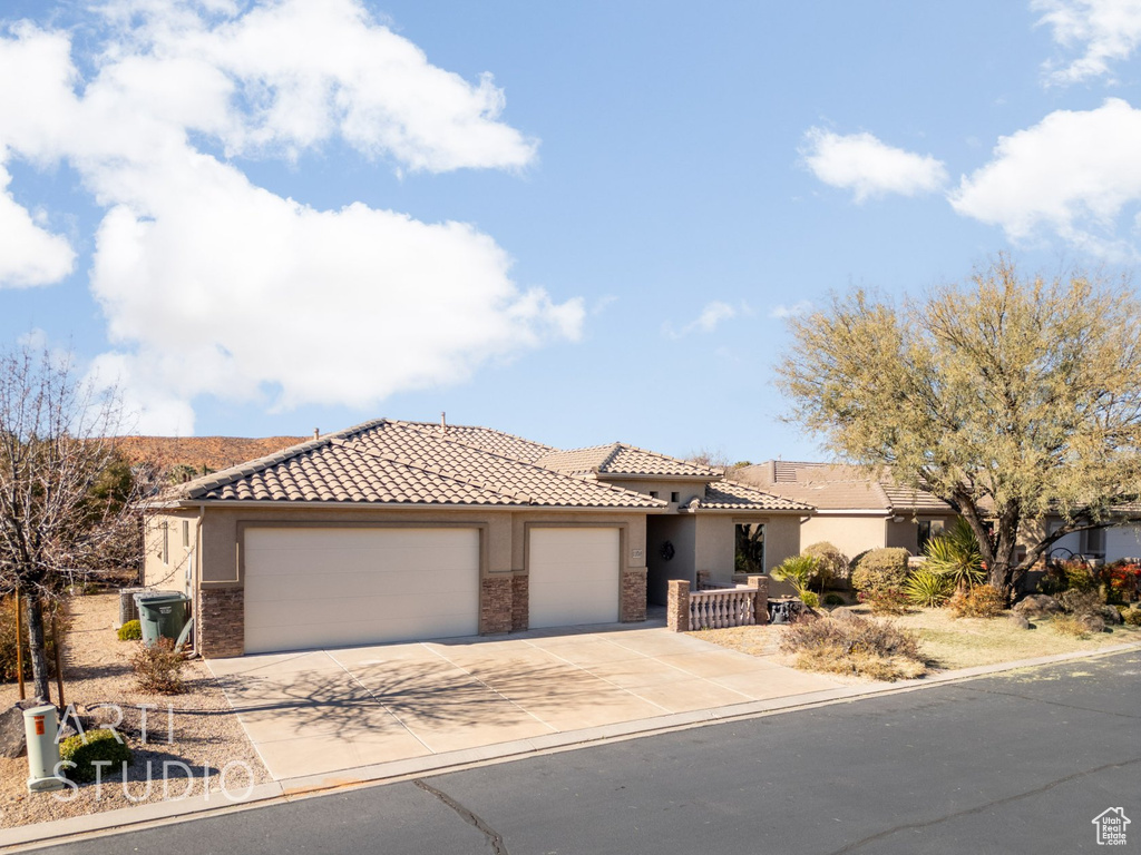Mediterranean / spanish house featuring stucco siding, an attached garage, a tile roof, stone siding, and concrete driveway