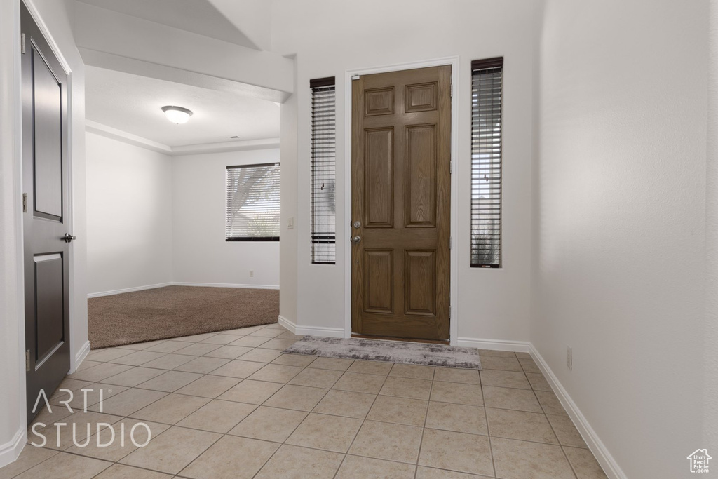 Foyer with light tile patterned flooring, light colored carpet, and baseboards
