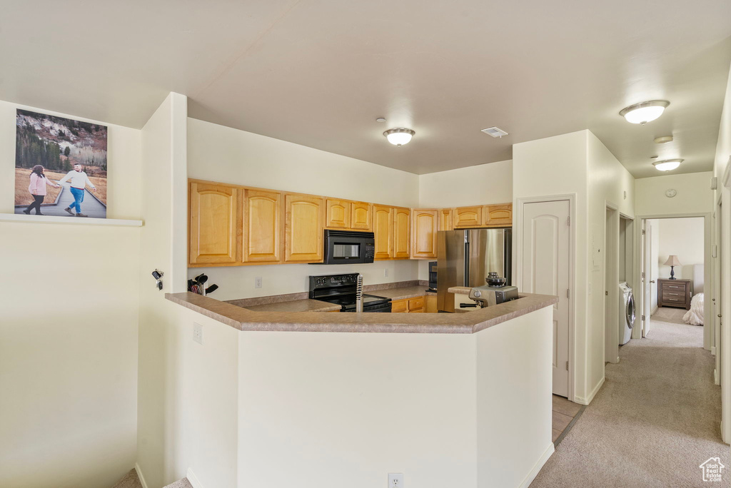 Kitchen featuring light carpet, a peninsula, washer and dryer, light countertops, and black appliances