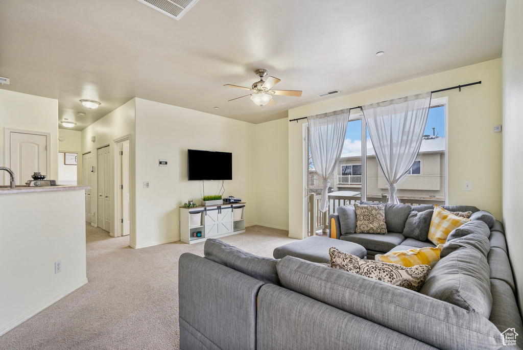 Living area with light carpet, baseboards, visible vents, and a ceiling fan